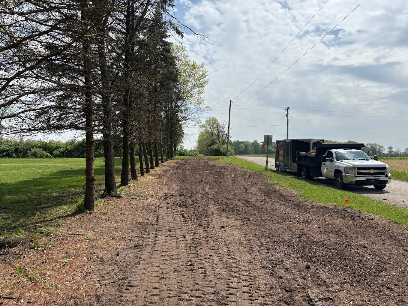 Cleared and graded tree line along a rural road with Worley's truck and dump trailer after a fence row cleanup